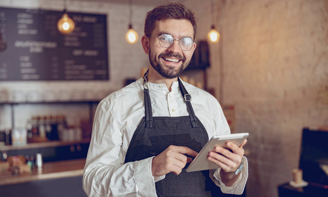 Un restaurateur qui pose souriant dans son restaurant avec une tablette de commande à la main