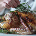 Un chef de cuisine qui pose une branche de romarin sur un poulet rôti