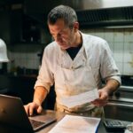 Chef-patron de restaurant français analysant l'écart entre marge théorique et marge réelle après le service, facture fournisseur en main